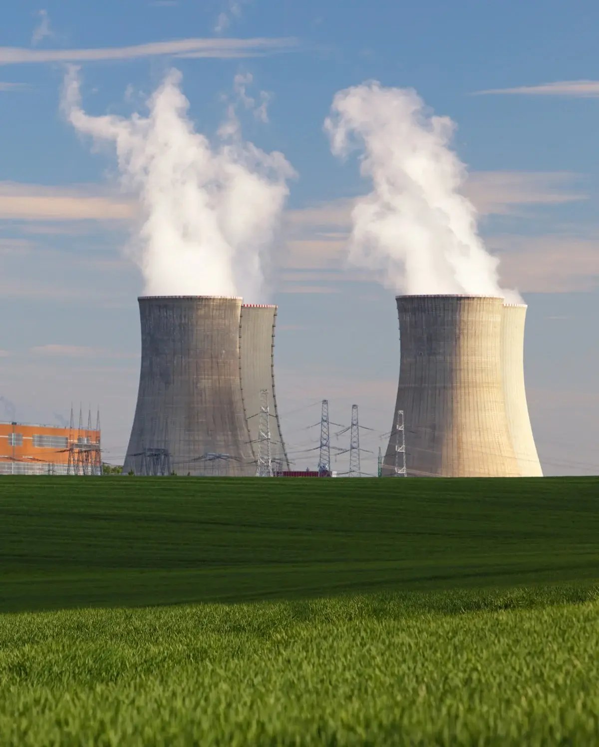 Two massive cooling towers of a nuclear power plant emitting steam, viewed from across a green field