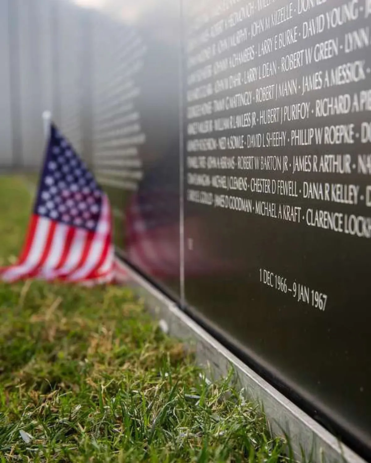 An American flag resting near the base of the Vietnam Veterans Memorial Wall, with names and dates engraved on the polished black granite An American flag resting near the base of the Vietnam Veterans Memorial Wall, with names and dates engraved on the polished black granite
