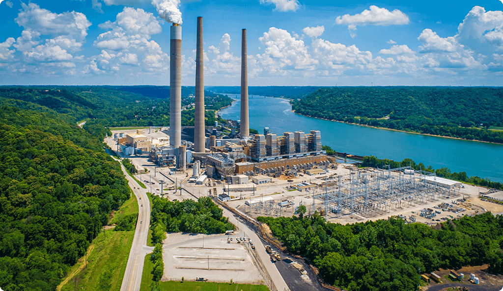 An aerial view of a large fossil fuel power plant with smokestacks, situated next to a river